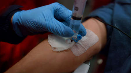 Medical worker in gloves inserting iv fluids into patient arm with catheter. Closeup paramedic...