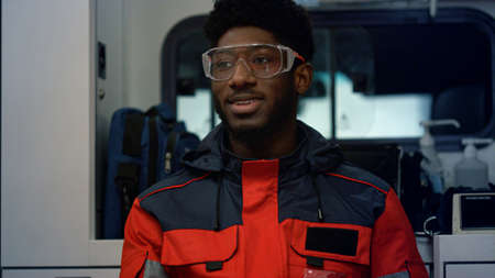 Emergency care assistant talking with colleague in ambulance car. Male paramedic waving head yes during conversation. African american doctor wearing medical uniform and protective glasses at workの写真素材