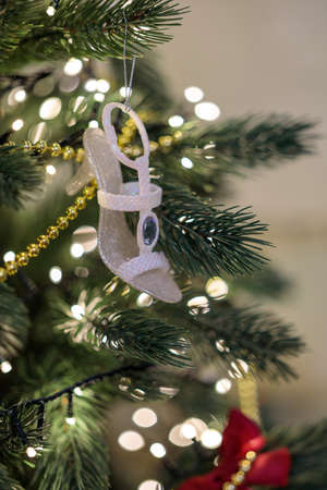 Closeup white shoe hanging on Merry Christmas tree. New year decor element at magic fir tree. Winter holiday decoration detail design. Festive xmas toy hanging pine tree branch shine golden garlandの写真素材