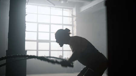 Athletic man doing fitness workout with battle ropes in sport club. Angry man training body in...