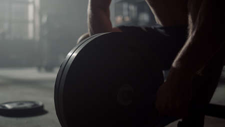 Closeup athletic man hands put heavy plates on barbell at fitness workout. Strong sportsman get ready at lifting weights training. Male athlete preparing sports equipment for strength exerciseの写真素材