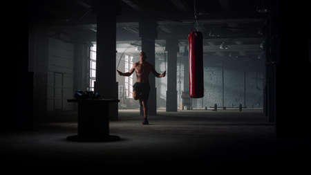 Male boxer jumping skipping rope in slow motion. Muscular man with naked torso warming up using jump...