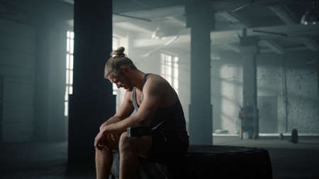 Tired sportsman sitting on big tire after functional training in sport club. Fitness man taking break between intense exercises in gym. Male bodybuilder posing at cameraの写真素材