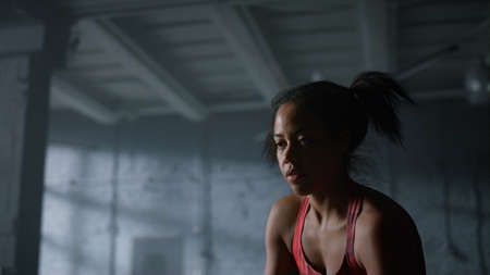 Portrait of strong sportswoman battling ropes in gym. African american woman using sports equipment...