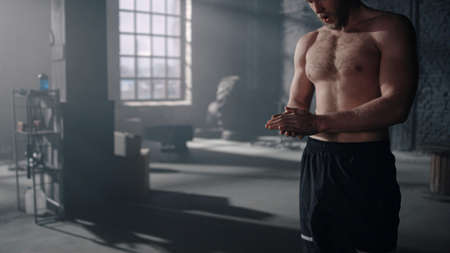 Muscular athlete finish fitness training barbell in dark gym. Powerful man taking break. Sports...
