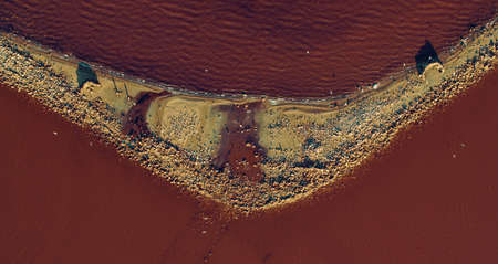 Pink sea waves splashing sandy beach at red water surface at summer. Top view salt mineral island at...