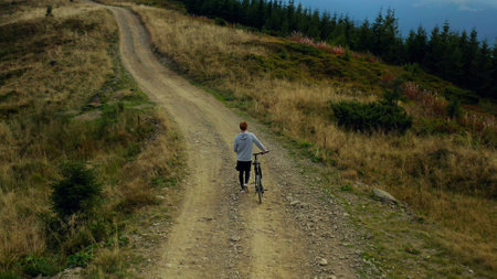 Man biking against mountains rocky road moving bike spring grass green trees. Charming tranquil scene active male cycling hills warm sunny day enjoying time drone view. Sport activity concept.の写真素材