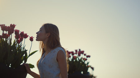 Beautiful woman profile smelling flowers in summer park outdoors. Gentle lady enjoying tulips in morning light outside. Smiling girl breathing in flower aroma in soft sunny light in blooming garden.の写真素材