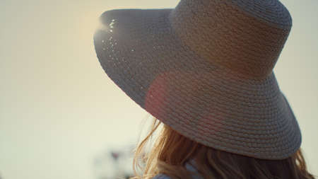 Beautiful woman in straw hat turning face to camera in sunlight outdoors. Portrait of young lady in...