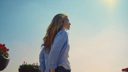 Closeup woman hands in pocket at walk in blooming garden outdoors. Young woman walking in spring park on blue sky background outdoor. Back view tourist girl with camera holding hands in jeans pockets.の写真素材