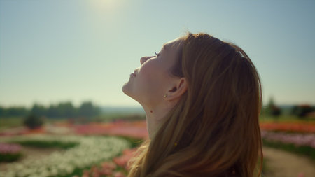 Silhouette of unknown woman enjoying spring sun light in flower garden. Calm woman profile standing...