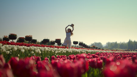 Happy woman enjoying flowers in tulip field. Young woman running in slow motion in spring flowers. Beautiful girl having joy in tulips park in daytime. Playful lady walking in tulip field.の写真素材