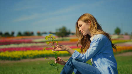 Young woman looking at rape branch in beautiful spring park in sunny day. Relaxed girl with long...
