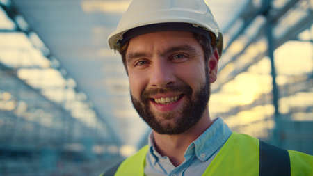 Portrait factory engineer smiling in camera enjoying work wearing white helmet. Professional happy...