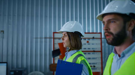 Uniformed manufacture specialists walking in warehouse discussing product. Focused handsome factory...