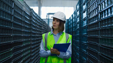 Woman warehouse employee examining blue supply boxes distribution walking. Focused handsome female storage specialist supervisor checking shipment pallets. Shipping goods export product conceptの写真素材