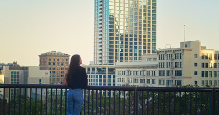 Unknown young lady walking on observation deck near high skyscraper back view. Unrecognized brunette...