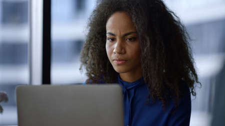 Serious african american woman executive working on laptop computer drinking morning coffee in home...