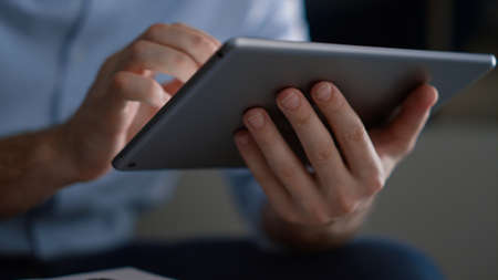 Business man hands using tablet computer surfing internet in home office. Unrecognizable ceo sitting holding digital device browsing social media in remote workplace. Corporate technology work conceptの写真素材