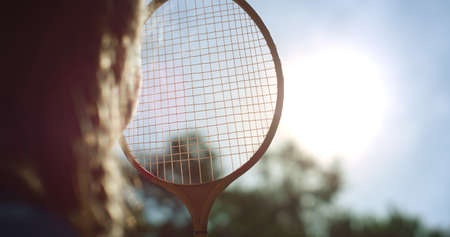 Closeup girl silhouette looking sun through badminton net alone in spring park. Unknown playful curious kid observing clear blue sky in warm sunlight. Summer vacation time. Carefree childhood conceptの写真素材