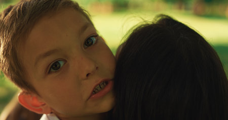 Pretty mother cuddling cute little boy on picnic close up. Cheerful young mom hugging smiling children on summer day green park. Happy moments family love. Spending time together outdoors.の写真素材