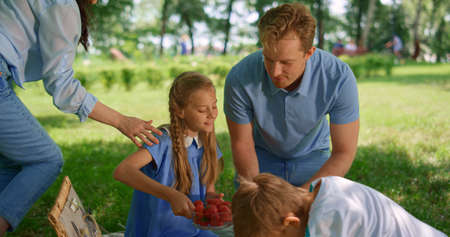 Happy family preparing healthy lunch on picnic in park green sunny lawn. Smiling parents taking...