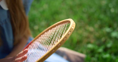 Closeup girl hand touching racket strings. Kid sitting on lush green lawn. Pensive blond child...