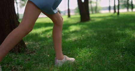 Running children legs on green grass sunny meadow. Unknown happy kids play outdoors near beautiful trees. Little feets jogging in sports shoes on lawn summerday. Active rest on family picnic concept.の写真素材
