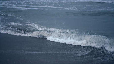 Blue water waves crashing coast background. Ocean foam splashing in dark sea landscape outdoors...