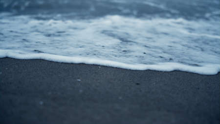White wave crashing beach sand. Blue sea water surface splashing on coastline environment. Dark...