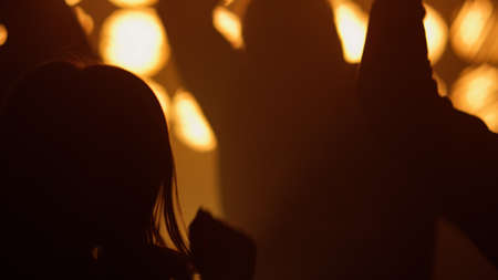 Concert crowd raising hands partying in night club. Happy cheering people jumping up in show spotlights. Silhouettes of cheerful dancing fans enjoying music in bright lights. Clubbing concept.の写真素材