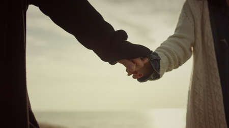 Dating lovers hold hands on sunrise sea beach nature. Couple touching arms outside close up....