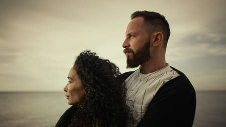 Couple standing sea beach on vacation. Multiethnic lovers hugging enjoying family trip vacation at ocean nature close up. Thoughtful young people looking away at shore island. Calmness love concept.の写真素材