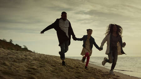 Playing family running coast at evening sea beach. People group have fun on sunset nature. Mother...