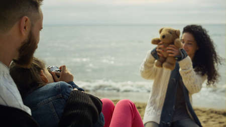 Family taking vacation pictures by sea beach. Dad mom kid rest on spring shore. Playful mother sitting posing camera on sand coast. Happy people enjoy relaxing holiday at nature. Leisure fun concept.の写真素材