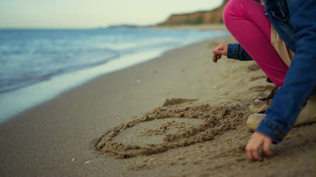Kid hands drawing sand beach at sea vacation. Unknown little girl playing on nature outside close up. Alone child touching ground at shore island. Daughter having fun on family trip. Childhood conceptの写真素材