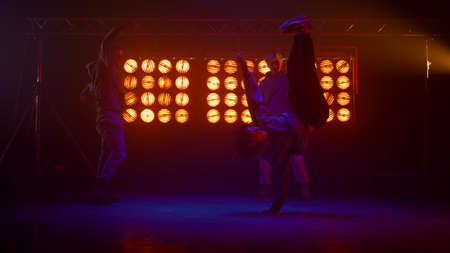 Breakdance crew making modern tricks on dancefloor nightclub. Silhouettes of breakdancing guys dancing freestyle elements on show stage. Stylish hip hop team battling on bright spotlights.の写真素材