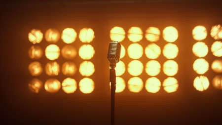 Vintage metal microphone standing empty stage in nightclub lights. Wonderful retro mic placed on concert scene lighted studio spotlights. View of musician equipment for recording music indoors.の写真素材