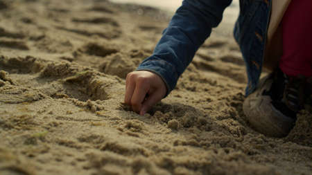 Happy child playing sand on ocean beach. Smiling kid having fun alone at shore. Adorable little girl digging ground at sea waves close up. Daughter enjoy family trip holiday. Childhood summer concept.の写真素材