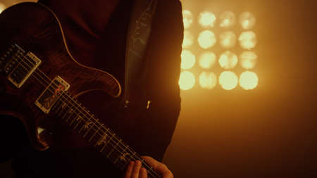 Professional guitarist holding electric guitar moving on stage nightclub close up. Man musical...
