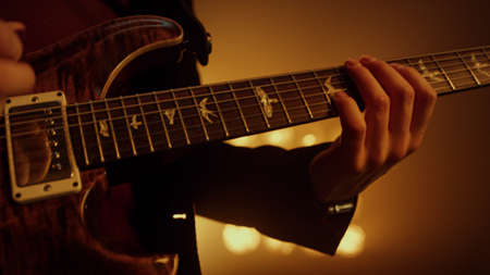Professional guitarist hands playing electric guitar on show stage night club. Close up musician...