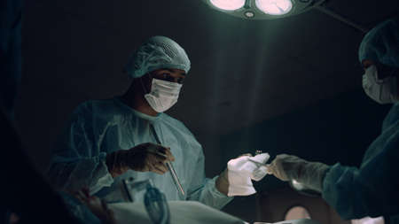 Serious surgeon performing surgical treatment in ward. Medical team cooperation. Nurse assisting...