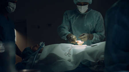 Nurse handling sterile instruments in dark room closeup. Medical team cooperation. African american man confident surgeon sterilizing patient skin before operation. Healthcare workers saving patient.の写真素材