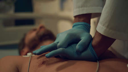 Closeup doctor doing heart massage to unconscious patient in hospital ward. Unknown healthcare worker saving man life performing cpr in emergency unit alone. Cardiac first aid in clinic room concept.の写真素材