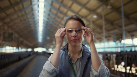Portrait livestock worker posing in cowshed. Agriculture manager put on glasses. Beautiful woman...