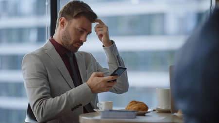 Focused entrepreneur sitting in cafe using cell phone surfing social media in office. Successful business man typing mobile message in corporate building. Professional communication online concept.の写真素材