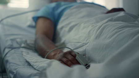 Ill man breathing oxygen mask in clinic ward. Pulse oximeter on finger closeup. Sleeping african american patient undergoing therapy in emergency hospital unit. Sick man lying resting in clinic room.の写真素材