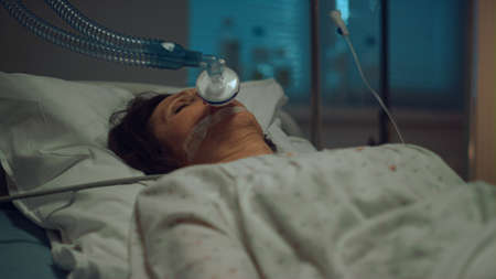 Patient with oxygen mask lying hospital bed in hospital intensive care unit. Unconscious woman...