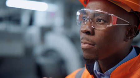 Closeup serious engineer moving hand at modern manufacturing factory. Portrait of uniformed african...