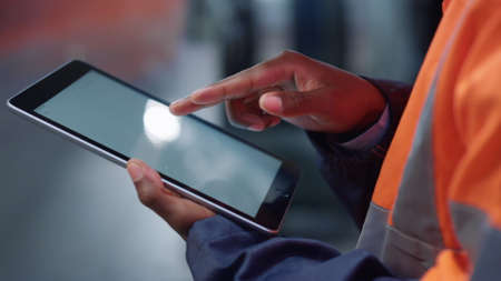 Close up supervisor hands scrolling tablet computer screen at modern manufacturing company. Unknown african american specialist tapping digital tab. Closeup industry technologies analyze data concept.の写真素材